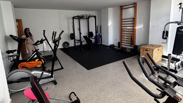 Et hjemmegymnasium med træningsudstyr, herunder en motionscykel, crosstrainer og vægtbænk.