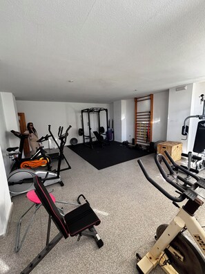 A home gym with exercise equipment including a stationary bike, elliptical, and weight bench.