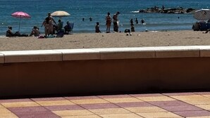En strand med mennesker, parasoller og en klippefyldt kystlinje.