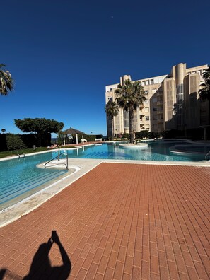 A swimming pool with a brick deck, surrounded by palm trees and a building with a modern design.