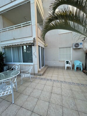 A covered outdoor area with a table and chairs, a small staircase, and a palm tree. - Beachfront apartment with private terrace, pool and parking (El Campello)