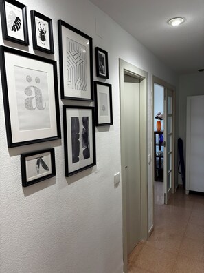 A hallway with framed artwork on the wall and a door leading to another room.