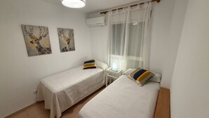 Et værelse med to enkeltsenge, et lille natbord med lampe, et vindue med let gardin og to billeder af hjorte på væggene.