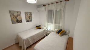 A room with two single beds, a small bedside table with a lamp, a window with sheer curtains, and two wall-mounted paintings of deer. - Beachfront apartment with private terrace, pool and parking (El Campello)
