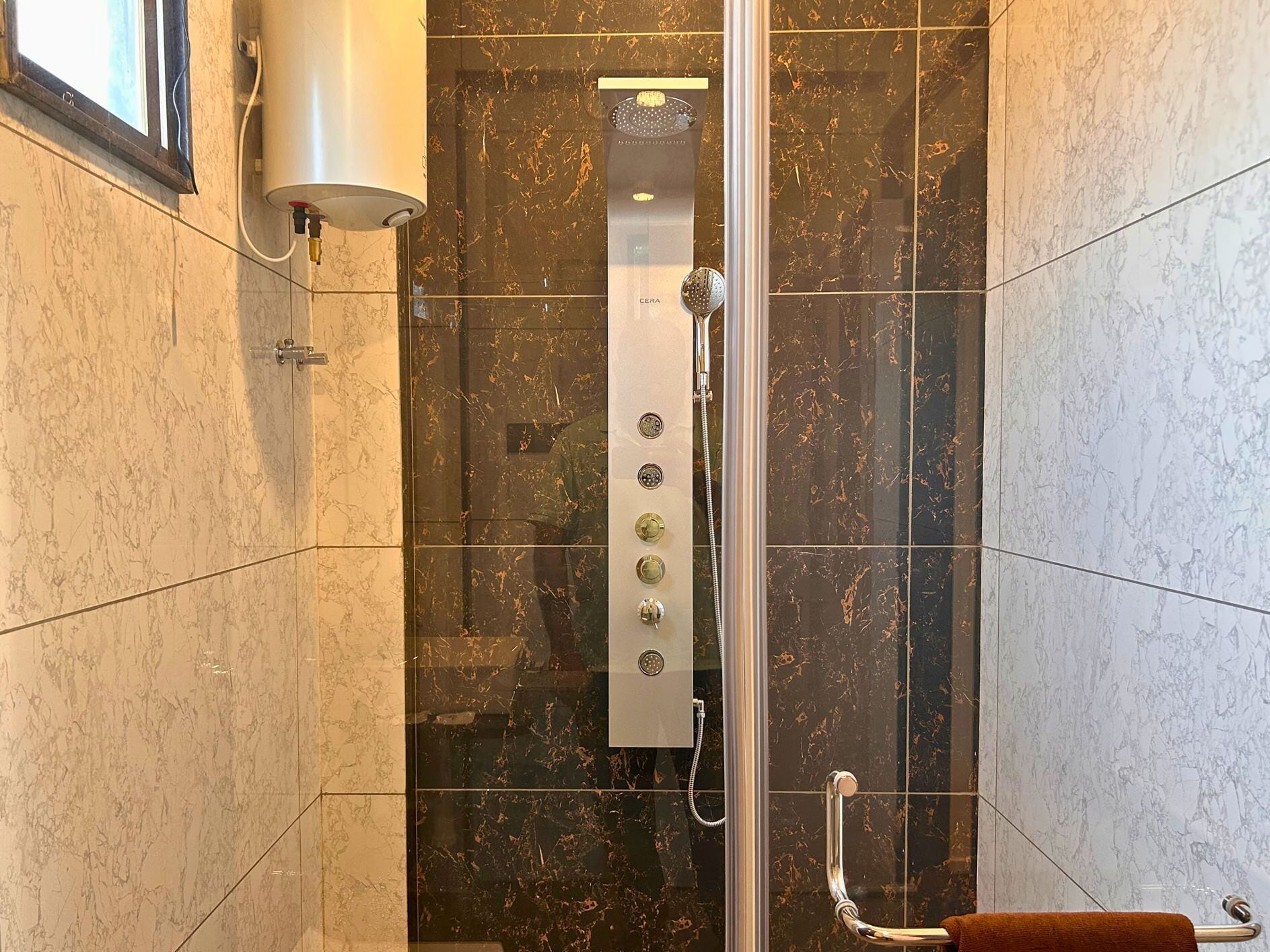 Un baño moderno con ducha de vidrio, azulejos de mármol y calentador de agua visible.