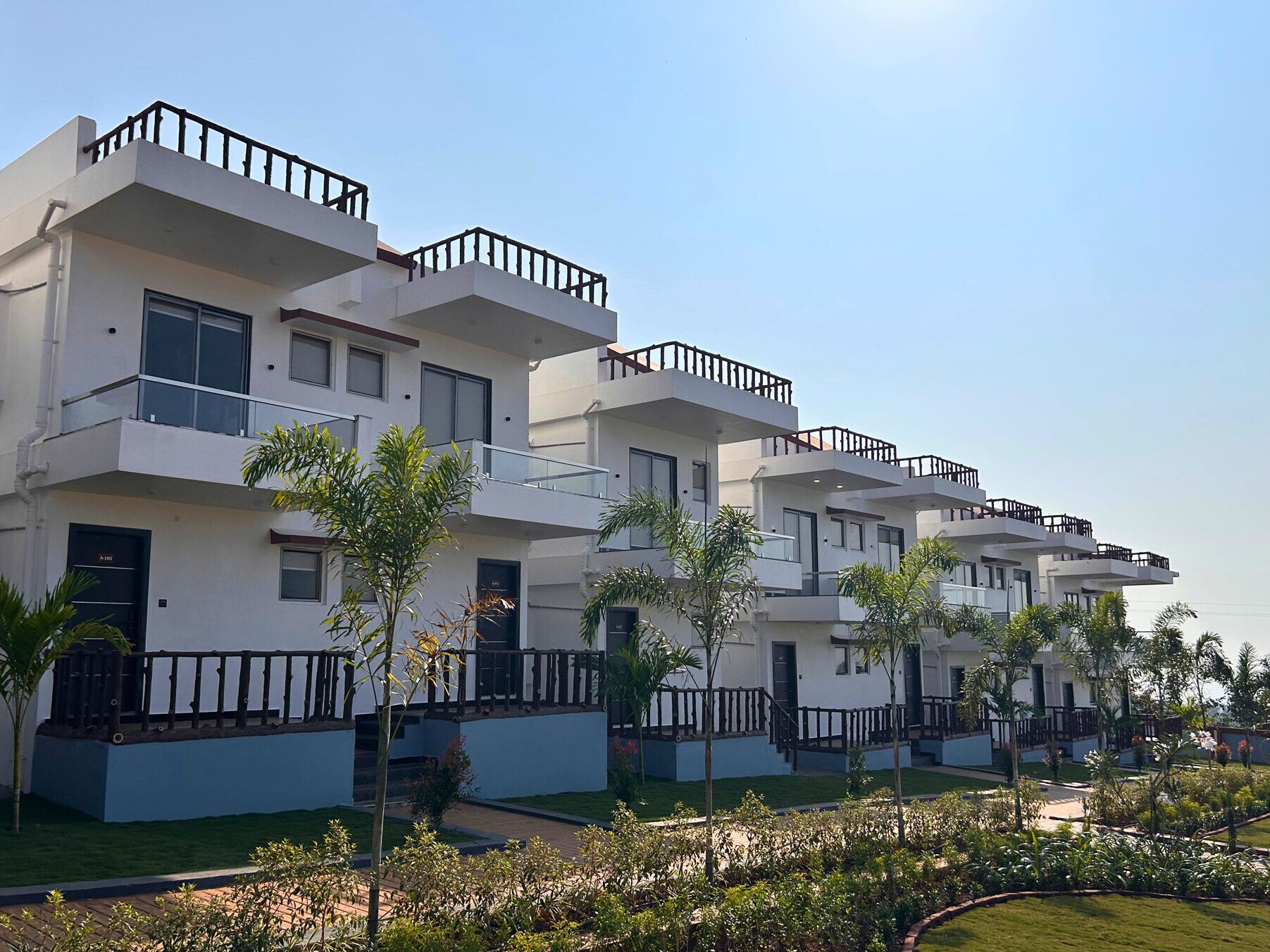 Un moderno edificio residencial de varios pisos con balcones y un jardín bien cuidado.