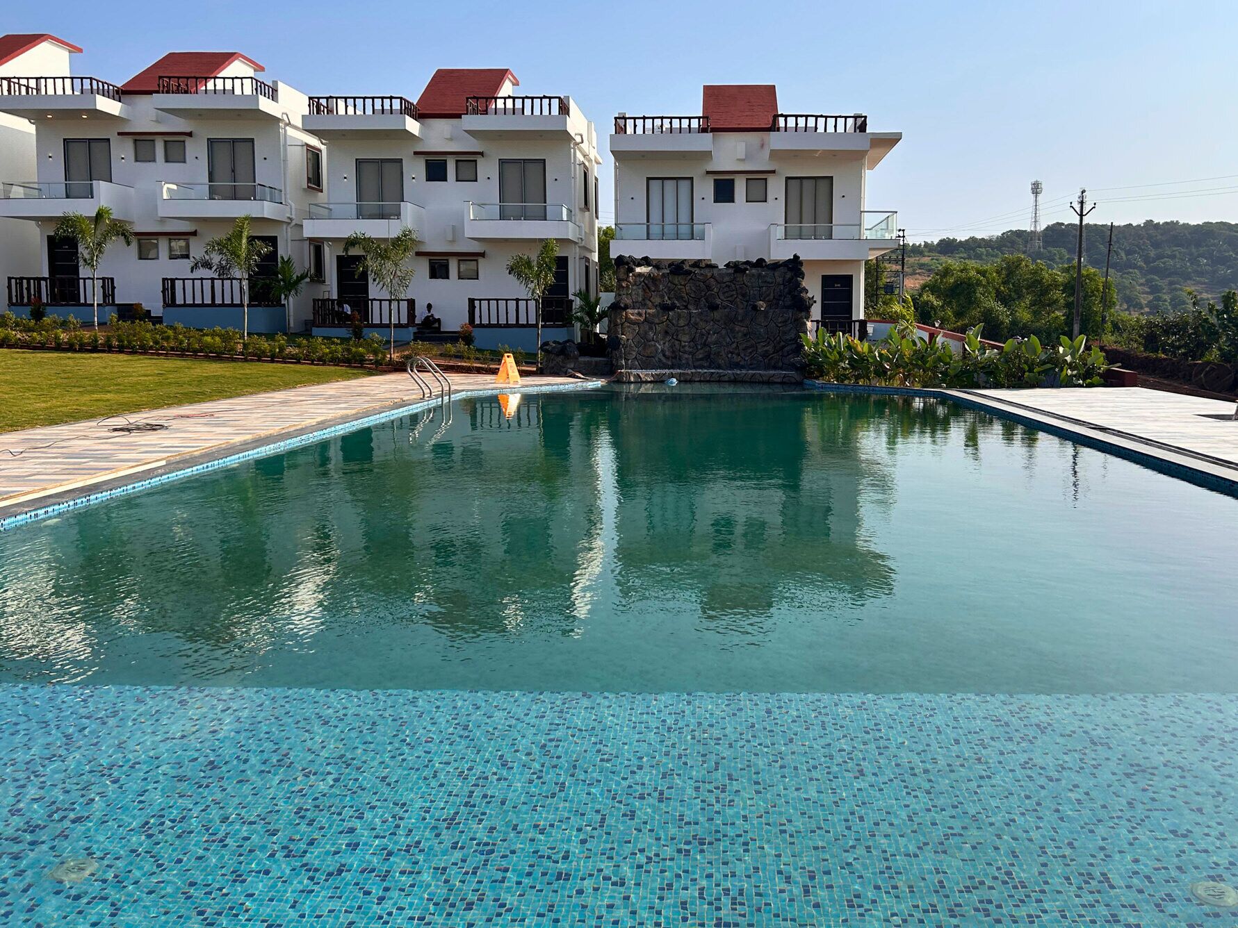 A swimming pool with a clear blue mosaic tile bottom, surrounded by a stone wall and a grassy area.