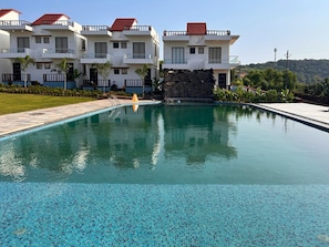 A swimming pool with a clear blue mosaic tile bottom, surrounded by a stone wall and a grassy area.