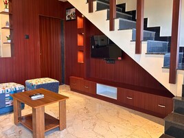 Una sala de estar moderna con una escalera de madera, un televisor de pantalla plana montado en la pared y una pequeña mesa de madera.