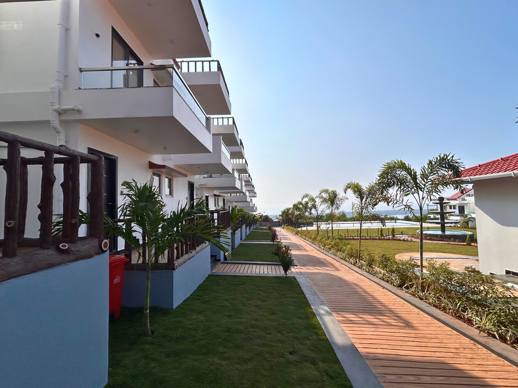 A hotel corridor with a wooden walkway, green lawn, and a view of the sea.
