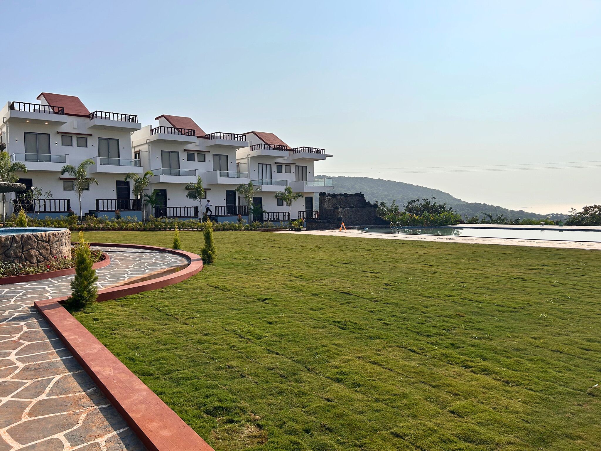 A modern building with multiple balconies, a swimming pool, and a well-maintained lawn.