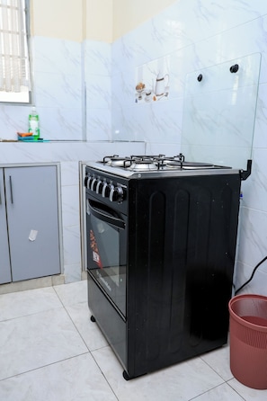 A kitchen with a black stove, grey cabinets, and a tiled backsplash. - Affordable 1 Bedroom Apartment in Utawala Nairobi Near JKIA (Nairobi)