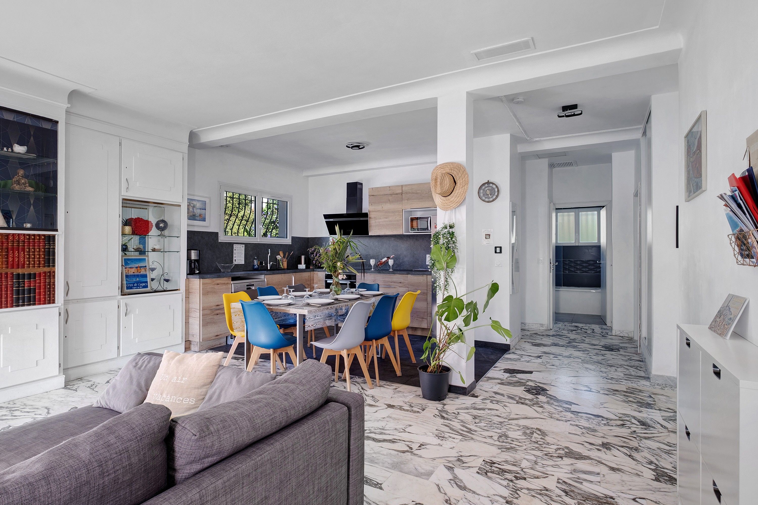 Ein modernes Wohnzimmer mit einem grauen Sofa, einem Essbereich mit blau und gelben Stühlen sowie einer Küche mit einer schwarzen Dunstabzugshaube.