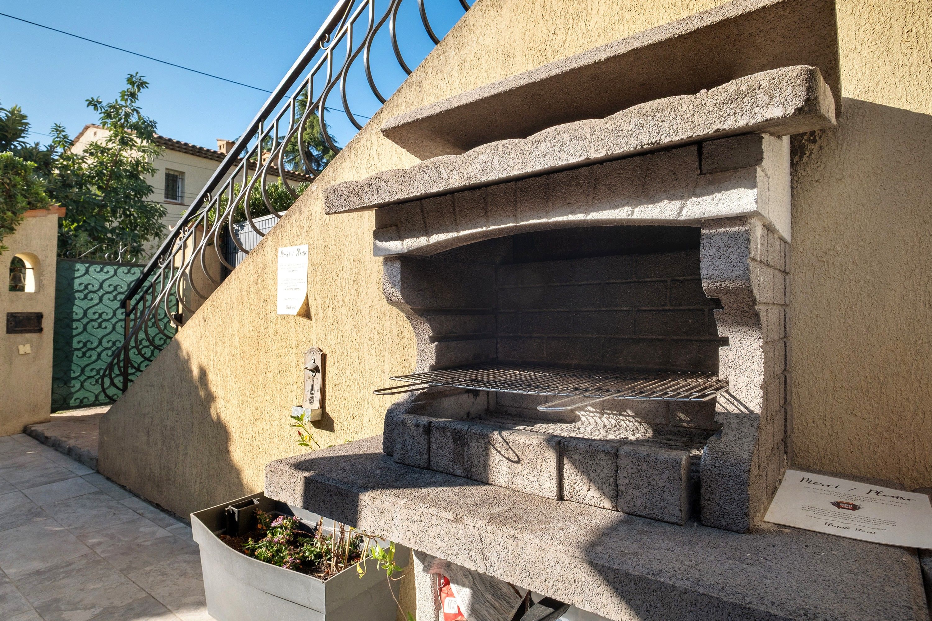 Barbecue in pietra esterna con griglia metallica, fioriera e ringhiera in metallo.