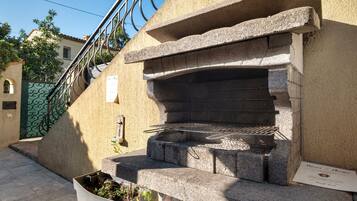Barbecue in pietra esterna con griglia metallica, fioriera e ringhiera in metallo.