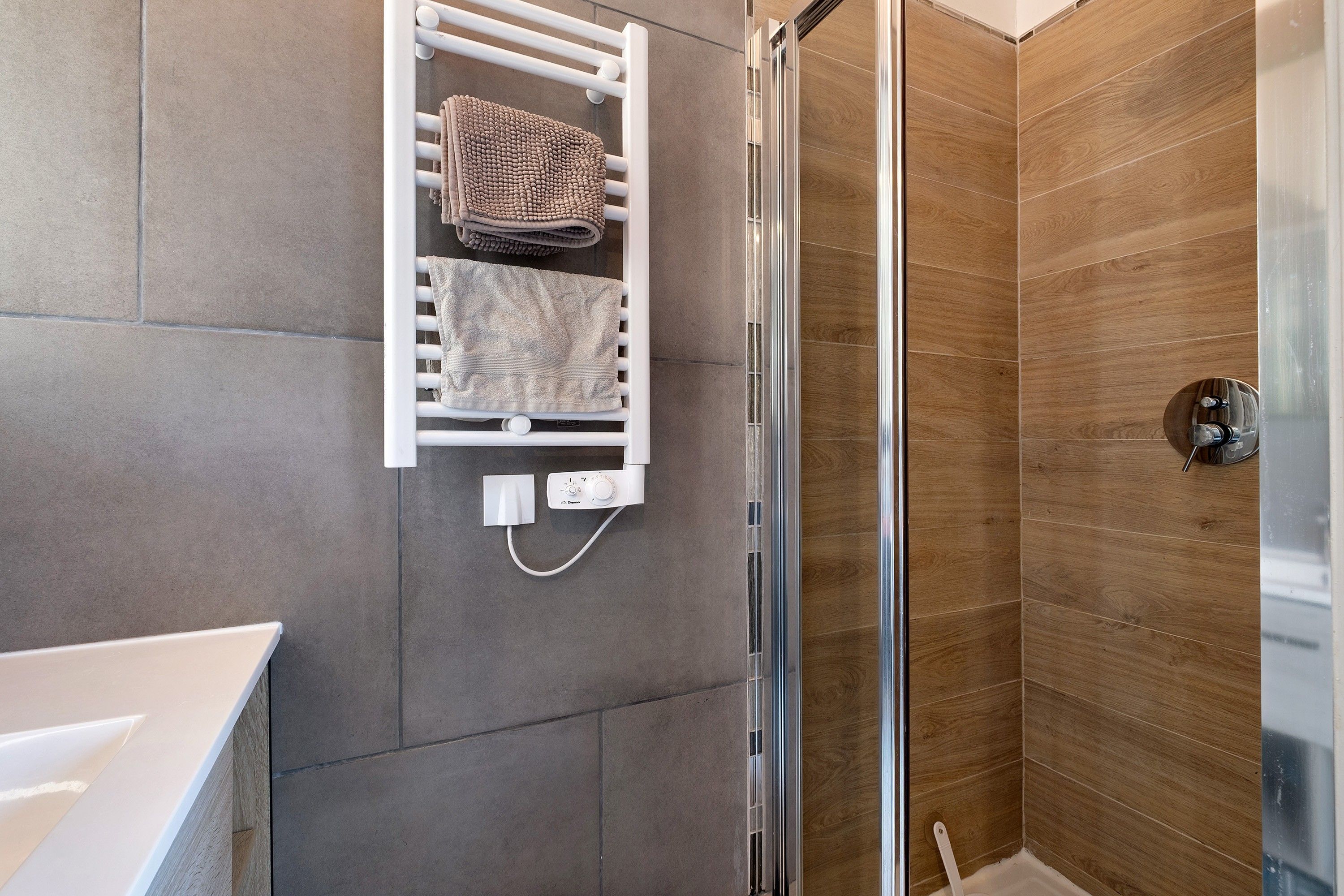 A bathroom with a shower, a towel rack, and a wall-mounted heater.