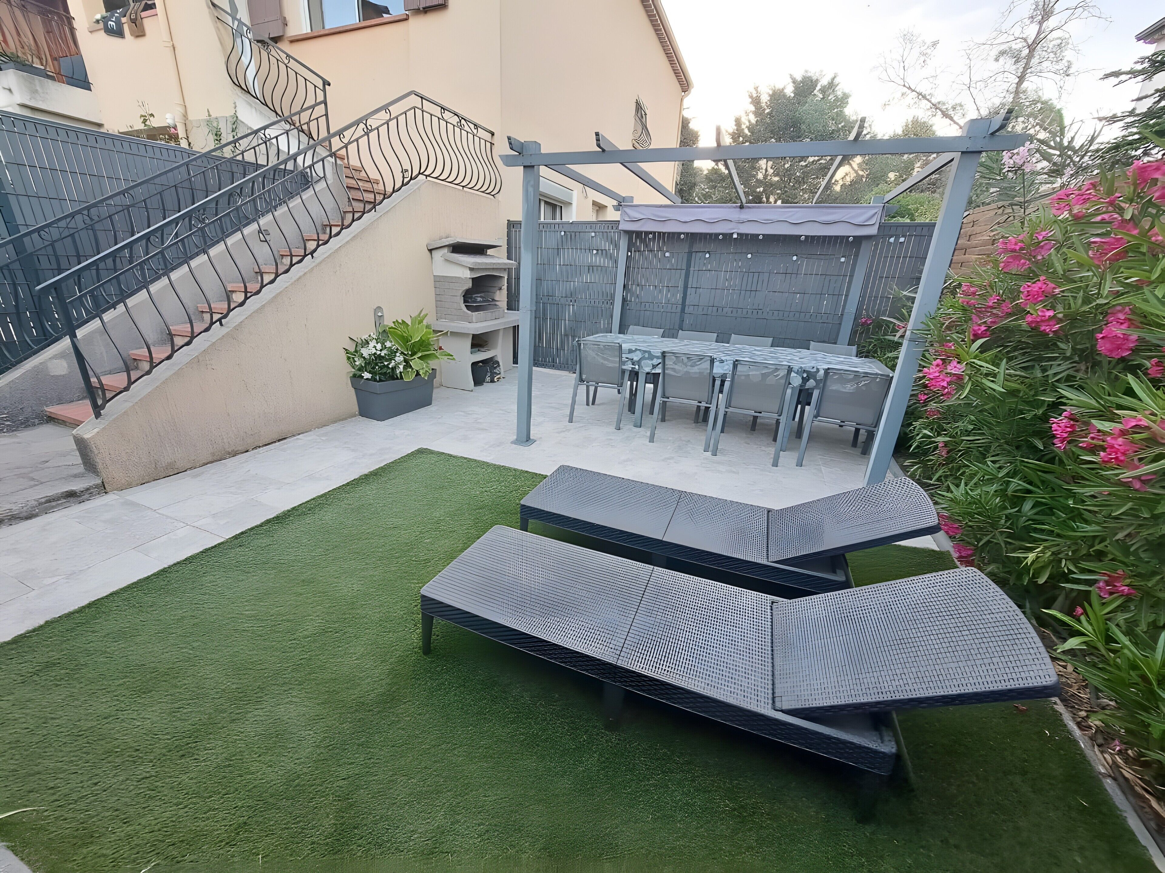A patio with a table and chairs, a small garden area with artificial grass, and a staircase.