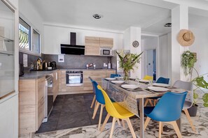 A modern kitchen with built-in appliances, a dining area with a marble table and colorful chairs, and a view of the outdoors. - Villa "Upper" – 3 bedrooms, 8 guests, private terrace, Wi-Fi, air conditioning (Cagnes-sur-Mer)