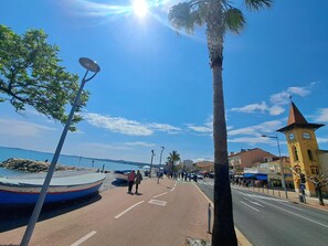 A coastal street with a pedestrian path, a palm tree, and a building with a clock tower. - Villa "Upper" – 3 bedrooms, 8 guests, private terrace, Wi-Fi, air conditioning (Cagnes-sur-Mer)