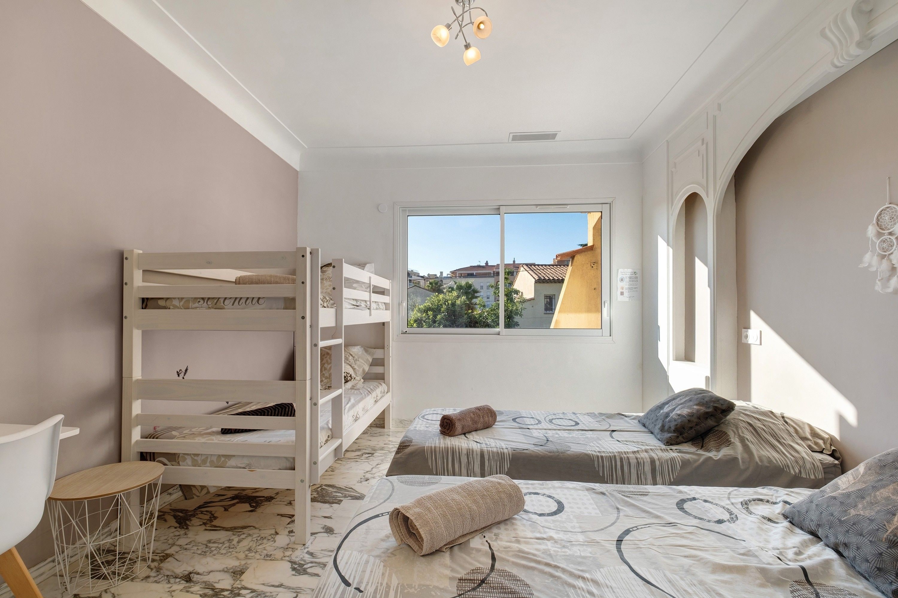 A bedroom with bunk beds, a desk, and a window with a view of buildings.