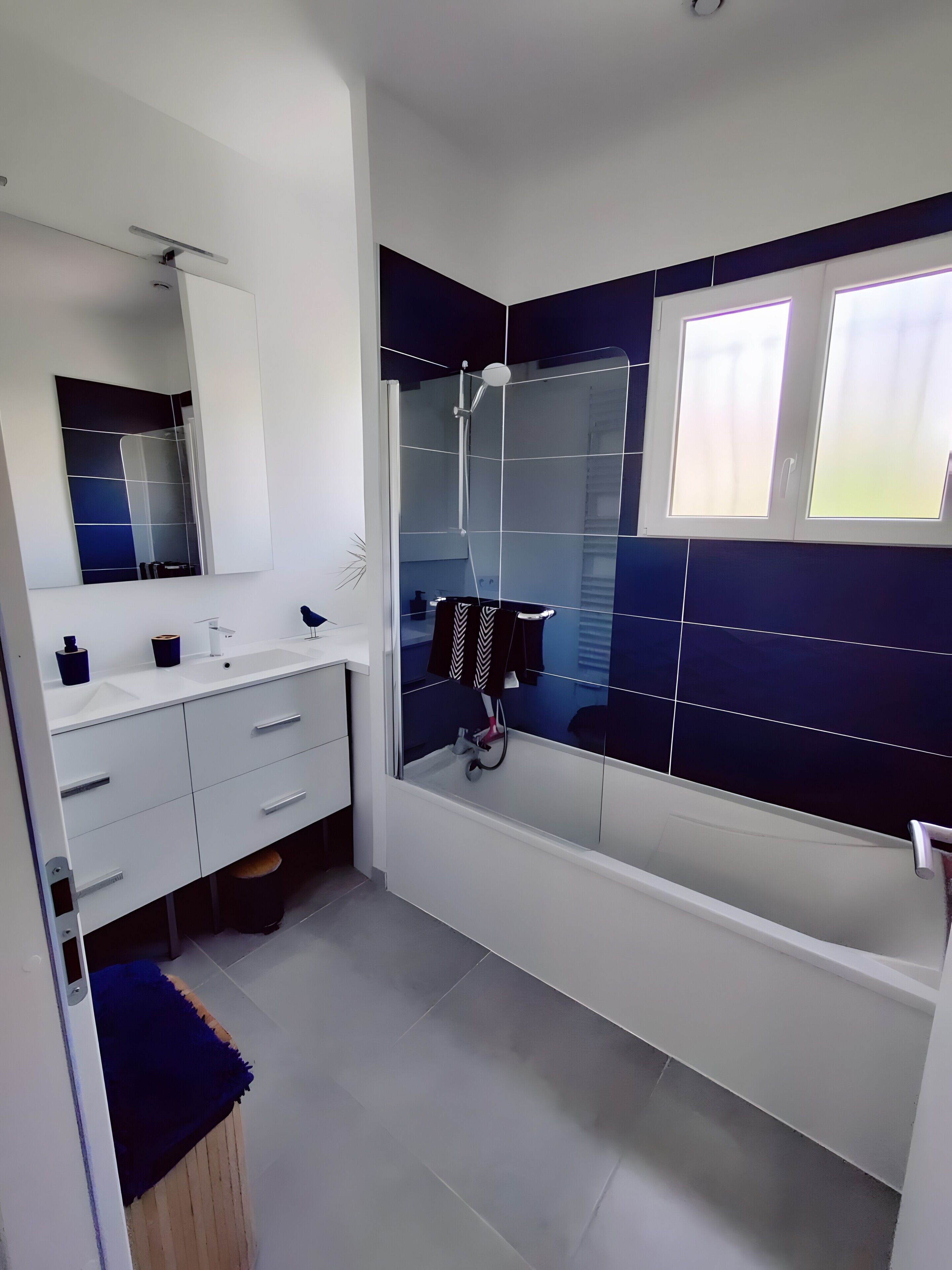 A modern bathroom with a white vanity, a glass-enclosed shower, and a large window.