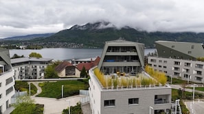 Un edificio moderno con techo plano, un patio central con asientos y vistas a un lago y montañas al fondo.