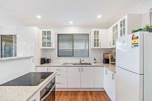 A modern kitchen with white cabinetry, a built-in oven, a sink, and a refrigerator. - Ideal for Tradies. BBQ, WiFi, Pet friendly (Torquay)