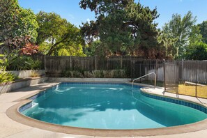 A rectangular swimming pool with a tiled edge, surrounded by a wooden fence, and various plants and trees in the background. - Disney, Heated Pool, Game Rm, Fire Pit, King Bed- Getaway Retreat (Hacienda Heights)