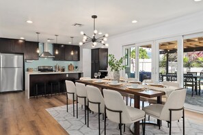 A modern kitchen with dark cabinets, a stainless steel refrigerator, and a dining area with a large table set for six. - Disney, Heated Pool, Game Rm, Fire Pit, King Bed- Getaway Retreat (Hacienda Heights)