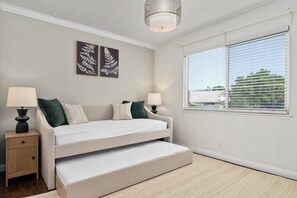 Ein Schlafzimmer mit einem Bett, zwei Nachttischen, zwei Lampen, einem Fenster mit Jalousien und zwei wandmontierten Dekorationen mit Blattmuster.