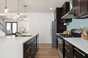 A modern kitchen with a central island, stainless steel appliances, and a view into the living area. - Disney, Heated Pool, Game Rm, Fire Pit, King Bed- Getaway Retreat (Hacienda Heights)