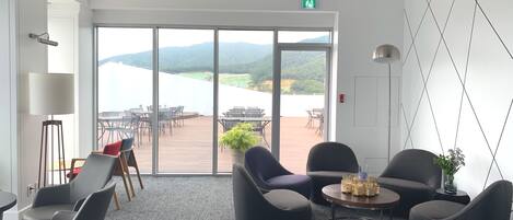 A modern interior with a view of a lake and mountains, featuring a seating area with a coffee table and chairs.
