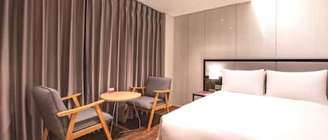 A hotel room with a bed, two armchairs, a small round table, and a nightstand with a lamp.