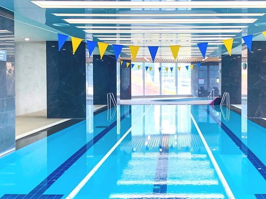 Una piscina con agua cristalina, rodeada de paredes de mármol oscuro y decorada con banderas azules y amarillas.