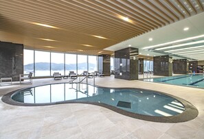 A modern indoor pool area with a view of mountains, lounge chairs, and a unique pool design.