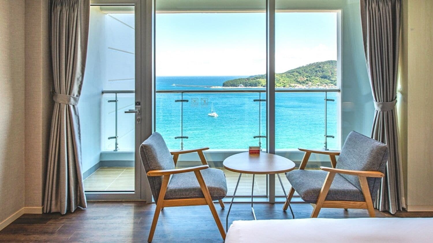 A hotel room with a balcony, two chairs, a small table, and a view of the sea.