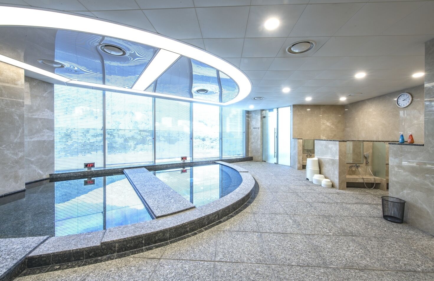 A modern indoor pool area with a glass barrier, a clock on the wall, and a view of the outside.