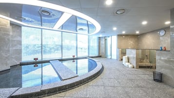 A modern indoor pool area with a glass barrier, a clock on the wall, and a view of the outside.