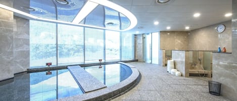 A modern indoor pool area with a glass barrier, a clock on the wall, and a view of the outside.