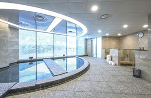 Un área de piscina interior moderna con barandilla de vidrio, un reloj en la pared y vistas al exterior.