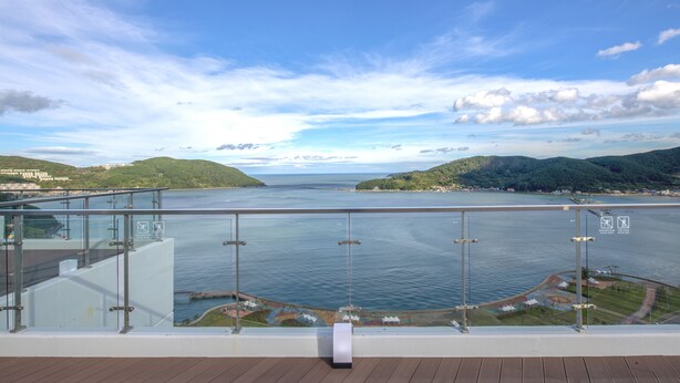 A panoramic view from a balcony overlooking a body of water, with a clear sky and distant hills.
