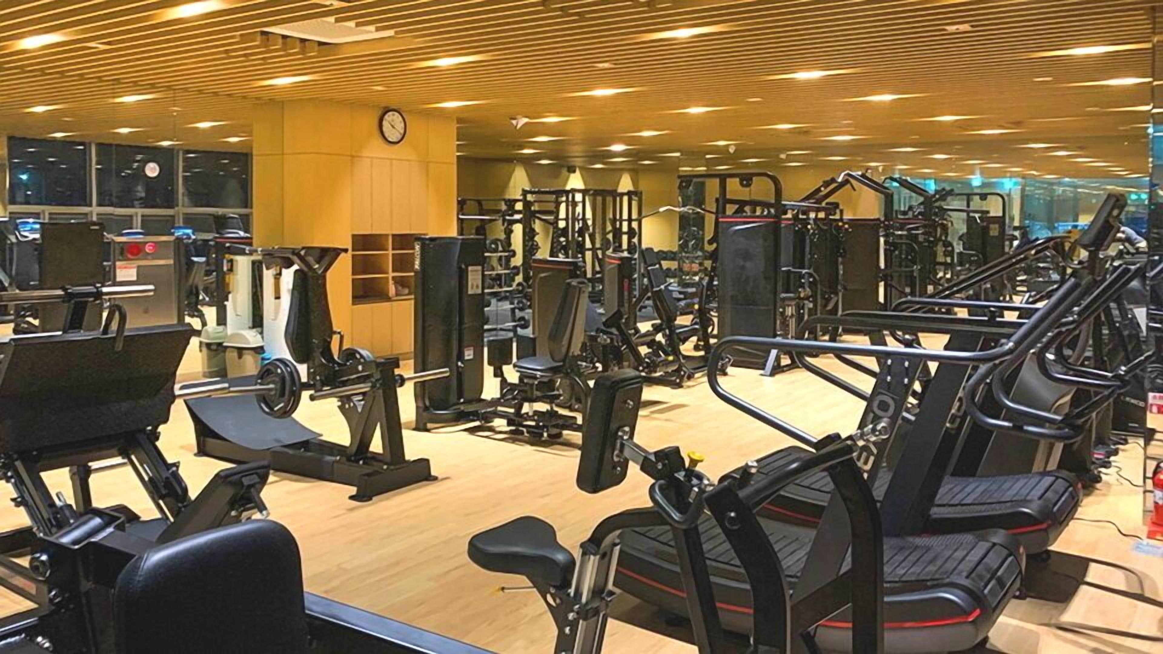 A gym with various exercise machines, including treadmills and weight stations, and a clock on the wall.