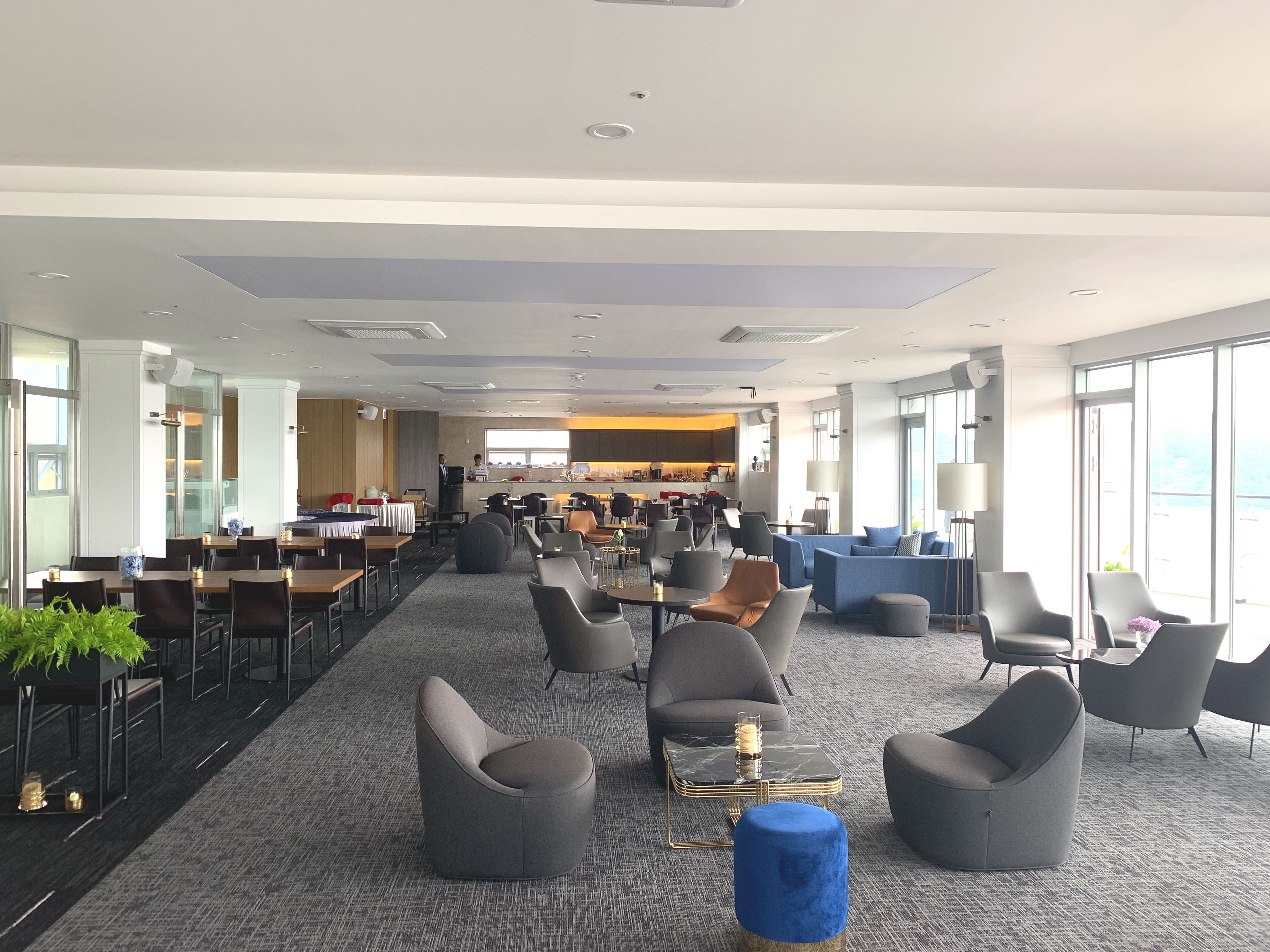 A spacious hotel lobby with multiple seating areas, a central bar, and large windows providing views.