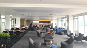 A spacious hotel lobby with multiple seating areas, a central bar, and large windows providing views.