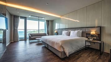 Una habitación de hotel moderna con una cama grande, un área de estar, una mesita de noche y vistas al mar.