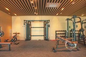 Un gimnasio con diversos equipos de ejercicio, incluyendo una estructura para sentadillas, bancos y accesorios para levantamiento de pesas.