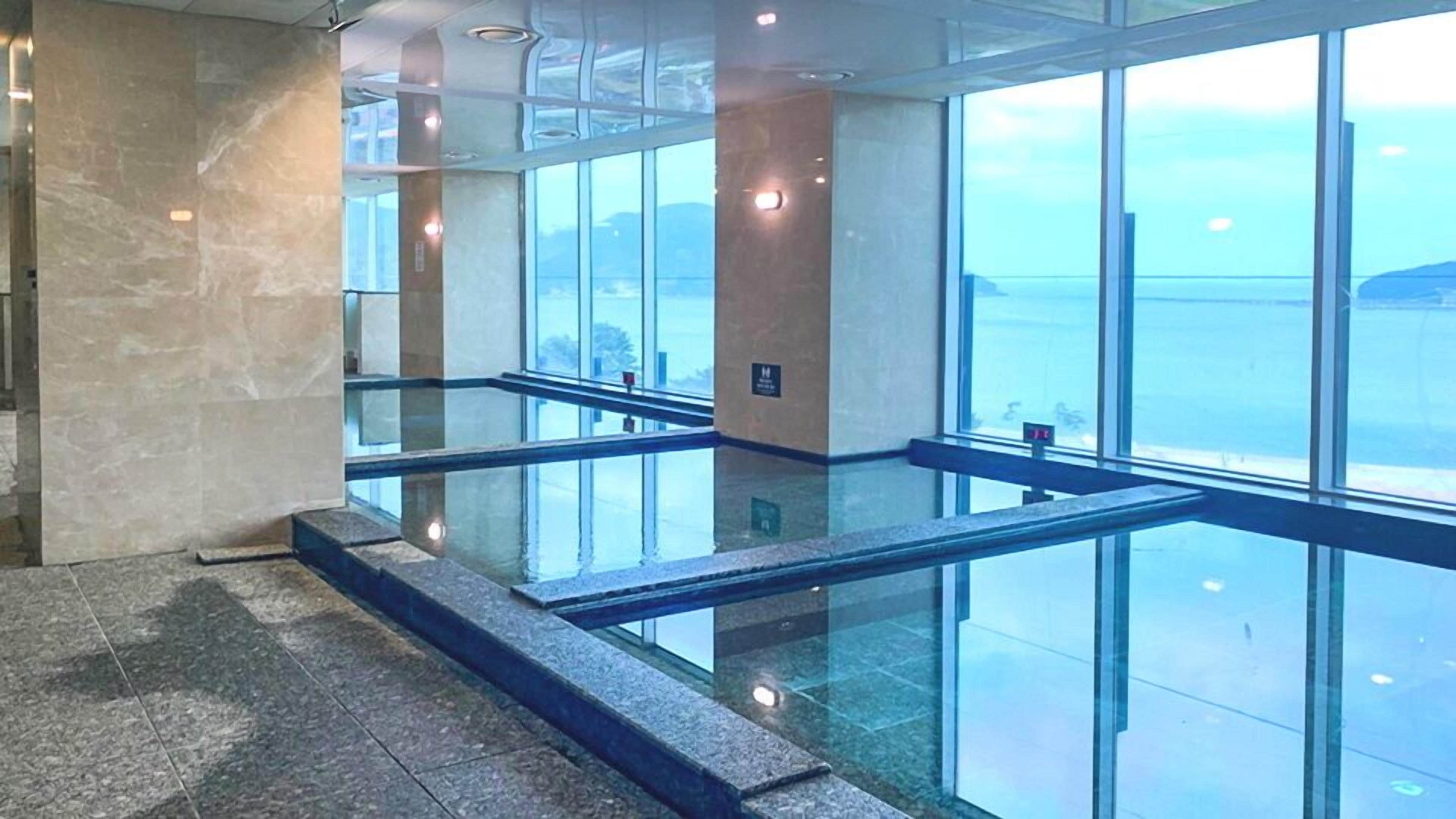 A modern interior with glass railings, a stone floor, and large windows offering a view.