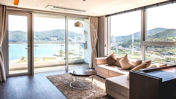 A modern living room with a sofa, a coffee table, and a view of a coastal landscape through large windows.