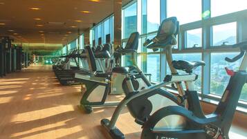 Un gimnasio con bicicletas estáticas y equipamiento de ejercicio, amplias ventanas y piso de madera.
