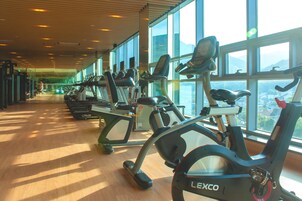 Un gimnasio con bicicletas estáticas y equipamiento de ejercicio, amplias ventanas y piso de madera.